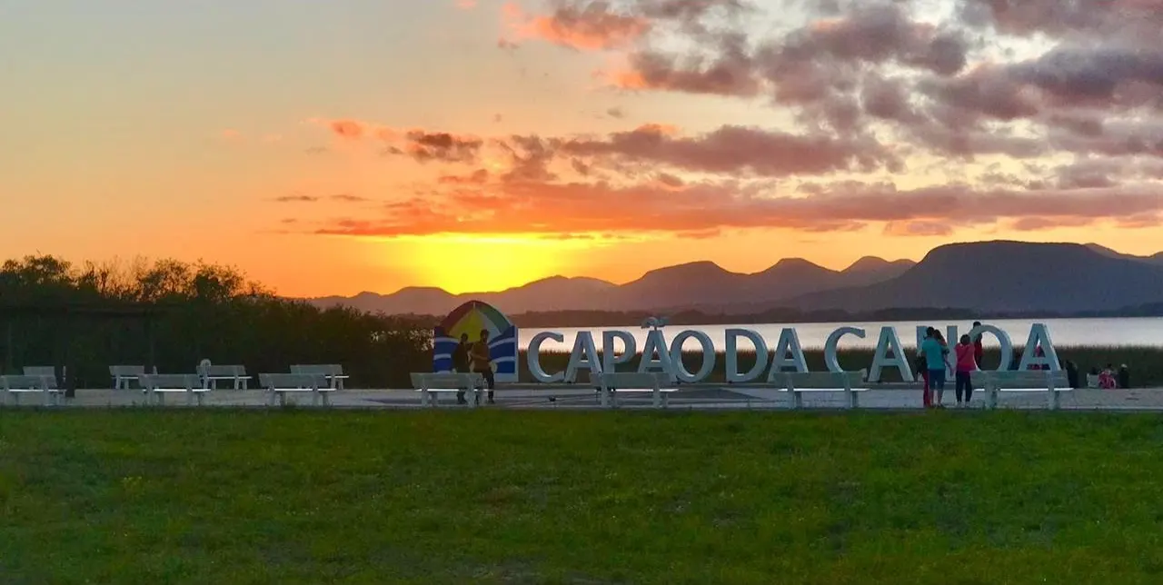 Pôr do sol sobre a lagoa e os morros, com o letreiro de Capão da Canoa.